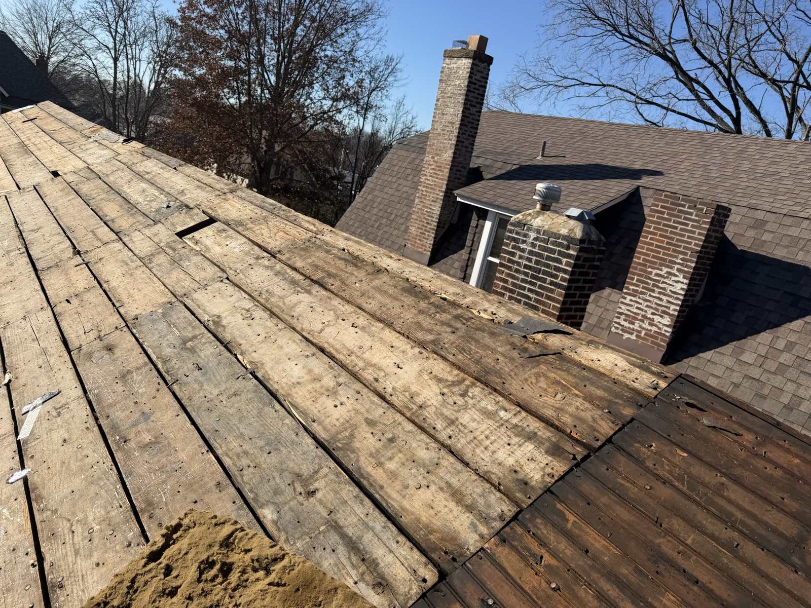 Open board decking on one slope of a house with two brick chimneys, the adjoining slope still shingled, under a clear winter sky