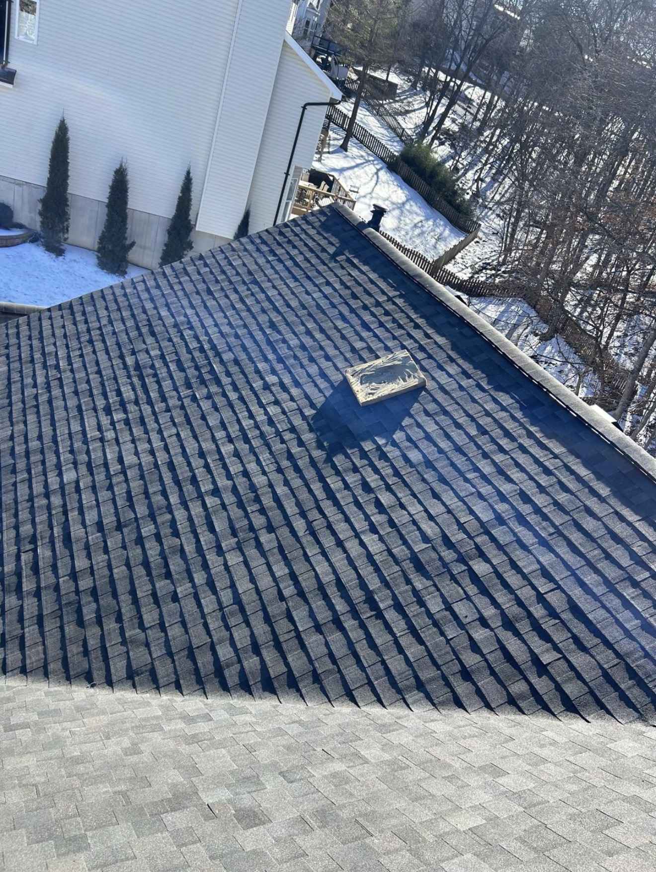 A dark shingle slope part way through installation with snow lying on the ground and along the fence line behind it